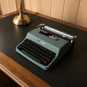Macchina da scrivere Olivetti Lettera 32 verde acqua su scrivania scura con bordo in legno e lampada in ottone.
