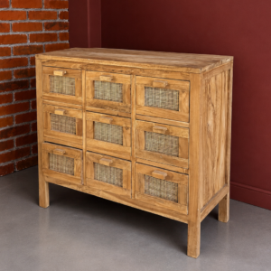 Cassettiera in legno di teak chiaro con nove cassetti, ciascuno con pannello frontale in rattan intrecciato, su sfondo rosso e mattone.