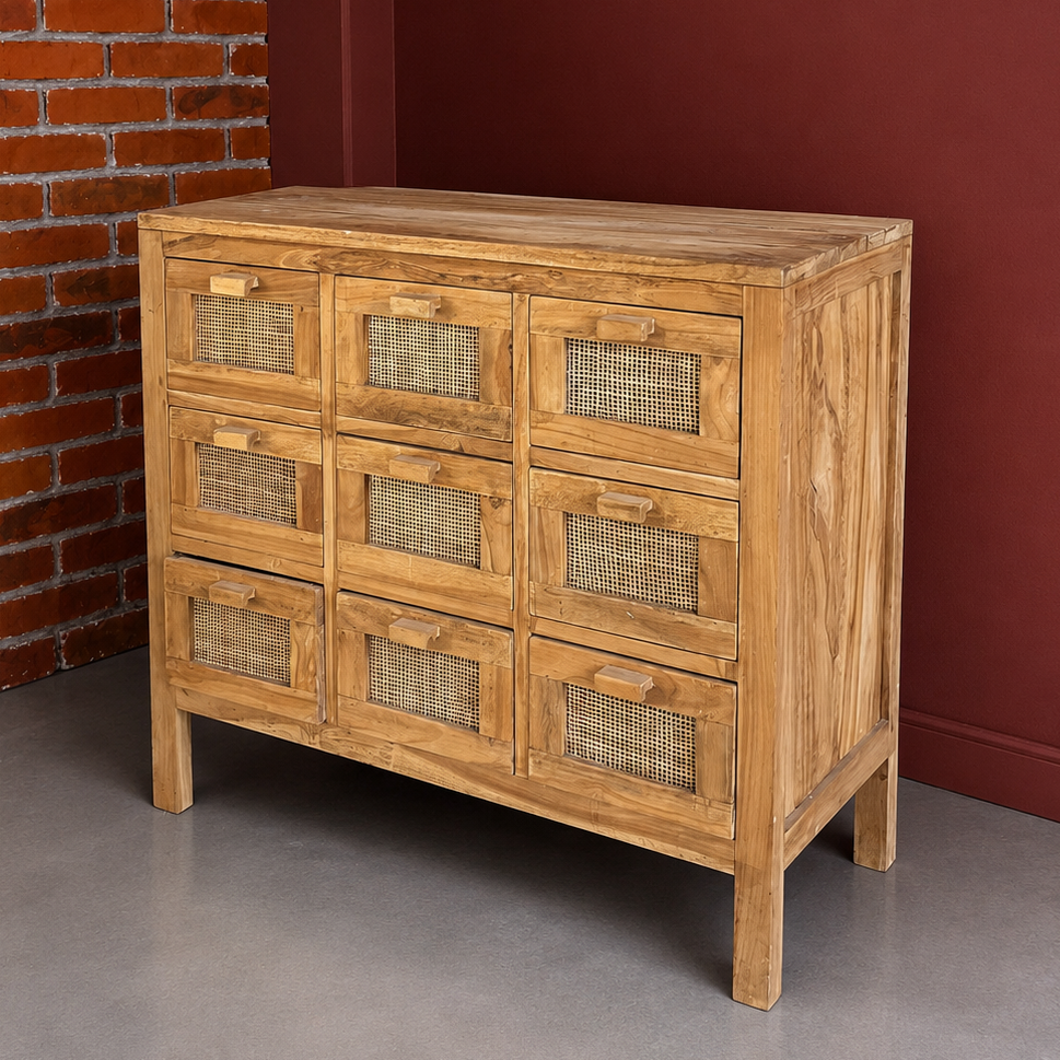 Cassettiera in legno di teak chiaro con nove cassetti, ciascuno con pannello frontale in rattan intrecciato, su sfondo rosso e mattone.
