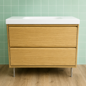Mobile lavabo moderno con due cassetti in legno chiaro, lavello bianco integrato e gambe metalliche, su sfondo di piastrelle verdi.
