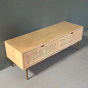 Mobile basso orizzontale in legno chiaro con due cassetti frontali in rattan intrecciato e quattro gambe sottili in metallo dorato, su sfondo grigio.