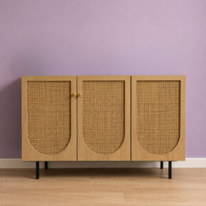 Credenza moderna a tre ante in legno chiaro con pannelli in rattan intrecciato e maniglie in ottone, su gambe nere, davanti a una parete lilla.