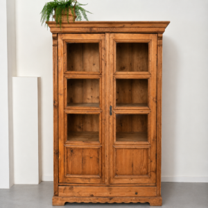 Vetrina in legno massello color miele con due ante a vetro divise in riquadri, dettagli intagliati e finitura rustica, su sfondo bianco.