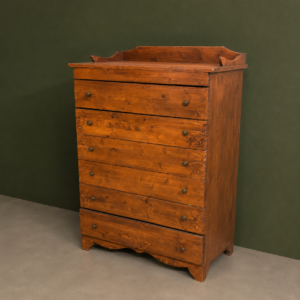 Cassettiera alta in legno massello di colore marrone rossiccio con sei cassetti, maniglie a pomello e intagli decorativi sulla base.