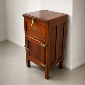 Ghiacciaia vintage in legno scuro con ferramenta in ottone lucido, posta in un angolo di una stanza moderna con pareti bianche.