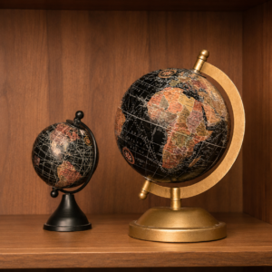 Due globi terrestri decorativi in stile antico, uno grande con base dorata e uno piccolo con base nera, su una mensola di legno.