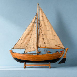 Modello di veliero in legno con scafo marrone e nero, vele beige in tessuto, su supporto in legno, sfondo blu.