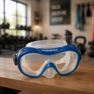 Maschera subacquea Tribord blu e trasparente con lenti in vetro temperato, posizionata su un tavolo di legno in una palestra.