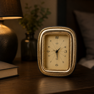 Orologio da tavolo vintage dorato con cassa ovale, quadrante crema e numeri arabi, su un comodino scuro.
