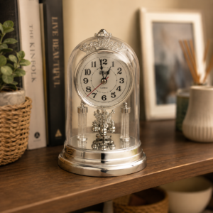 Orologio da tavolo decorativo con cupola trasparente e base argentata lucida, posizionato su una mensola di legno.
