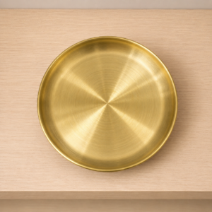 Vassoio rotondo in ottone spazzolato con finitura dorata e texture concentrica, posizionato su una superficie di legno chiaro.