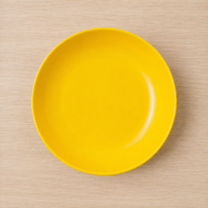 Piatto piano rotondo di colore giallo brillante con finitura lucida, posizionato su una superficie di legno chiaro.