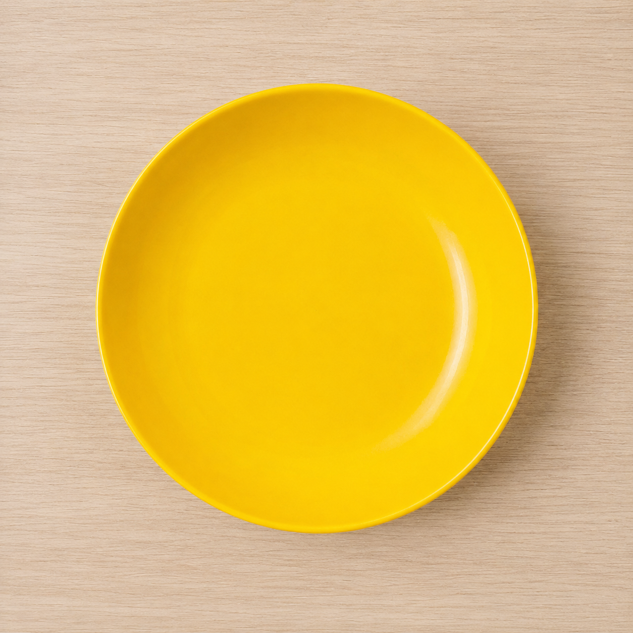 Piatto piano rotondo di colore giallo brillante con finitura lucida, posizionato su una superficie di legno chiaro.