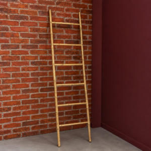 Scala decorativa in bambù naturale appoggiata a una parete di mattoni rossi e una parete bordeaux in un ambiente loft.