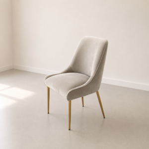 Sedia imbottita moderna in velluto beige chiaro con schienale curvo e quattro gambe affusolate color oro, su pavimento chiaro.