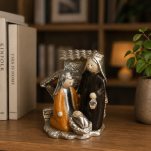 Natività stilizzata moderna con figure di Maria, Giuseppe e Gesù Bambino in finitura argento, arancione e marrone, su scaffale di legno.