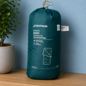 Sacco a pelo Quechua Basic di colore verde scuro, riposto nella sua sacca di compressione, su una mensola di legno.