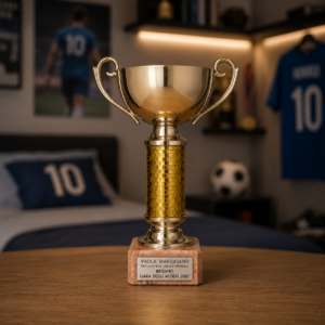 Trofeo dorato lucido con manici ricurvi e fusto decorato, poggiato su una base di marmo con targa incisa.