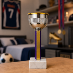 Trofeo sportivo con coppa argentata e bordo dorato, fusto viola e oro, su base di marmo bianco, in un ambiente sfocato.