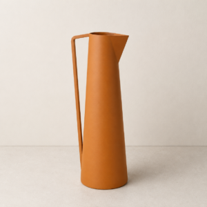 Brocca decorativa alta e slanciata di colore arancio terracotta opaco, con manico geometrico, su sfondo neutro.