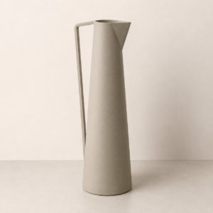 Brocca decorativa alta e slanciata, di colore grigio-beige opaco, con manico geometrico, su sfondo neutro.