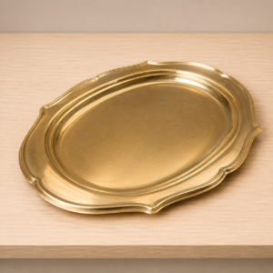 Vassoio ovale in ottone lucido con bordo decorato, posizionato su una superficie di legno chiaro.