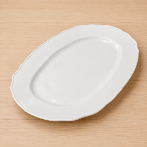 Piatto da portata ovale in ceramica bianca con bordo ondulato, posizionato su una superficie di legno chiaro.